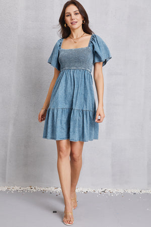 Light denim prairie dress with smocked bodice, puff sleeves, and tiered skirt.