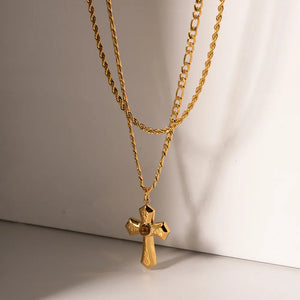 Gold layered chain necklace with a sculpted cross pendant featuring a central stone.