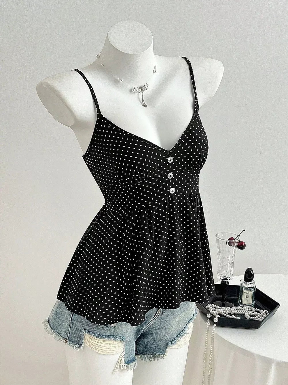 Black polka dot peplum cami with spaghetti straps and button front, styled with denim shorts.