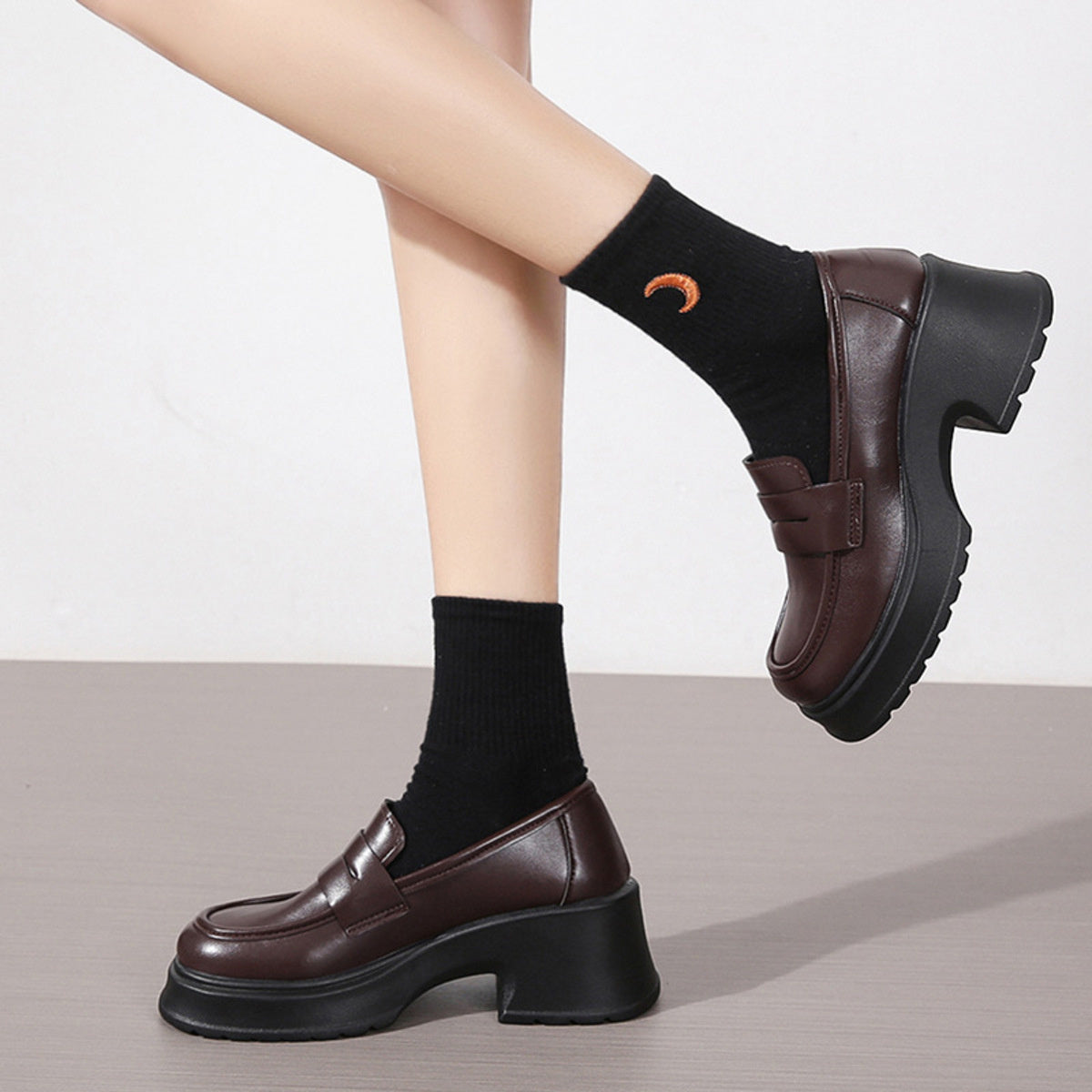 Dark brown round toe loafers with chunky block heels and black socks.