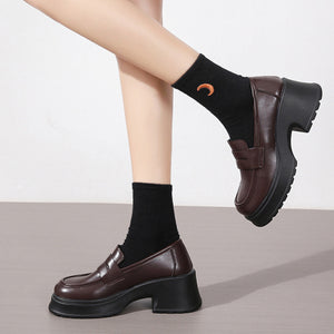 Dark brown round toe loafers with chunky block heels and black socks.