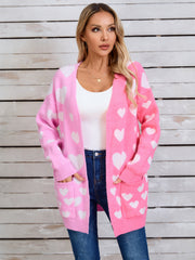 Pink open cardigan with white heart pattern, featuring pockets and a relaxed fit.