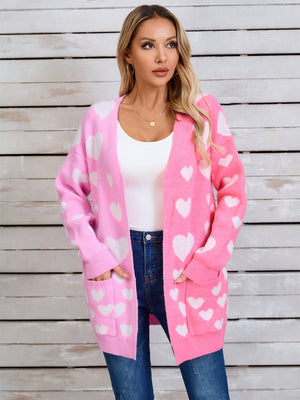 Pink open cardigan with white heart pattern, featuring pockets and a relaxed fit.