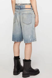 Distressed denim bermuda shorts in medium wash with paint splatters and frayed hem.