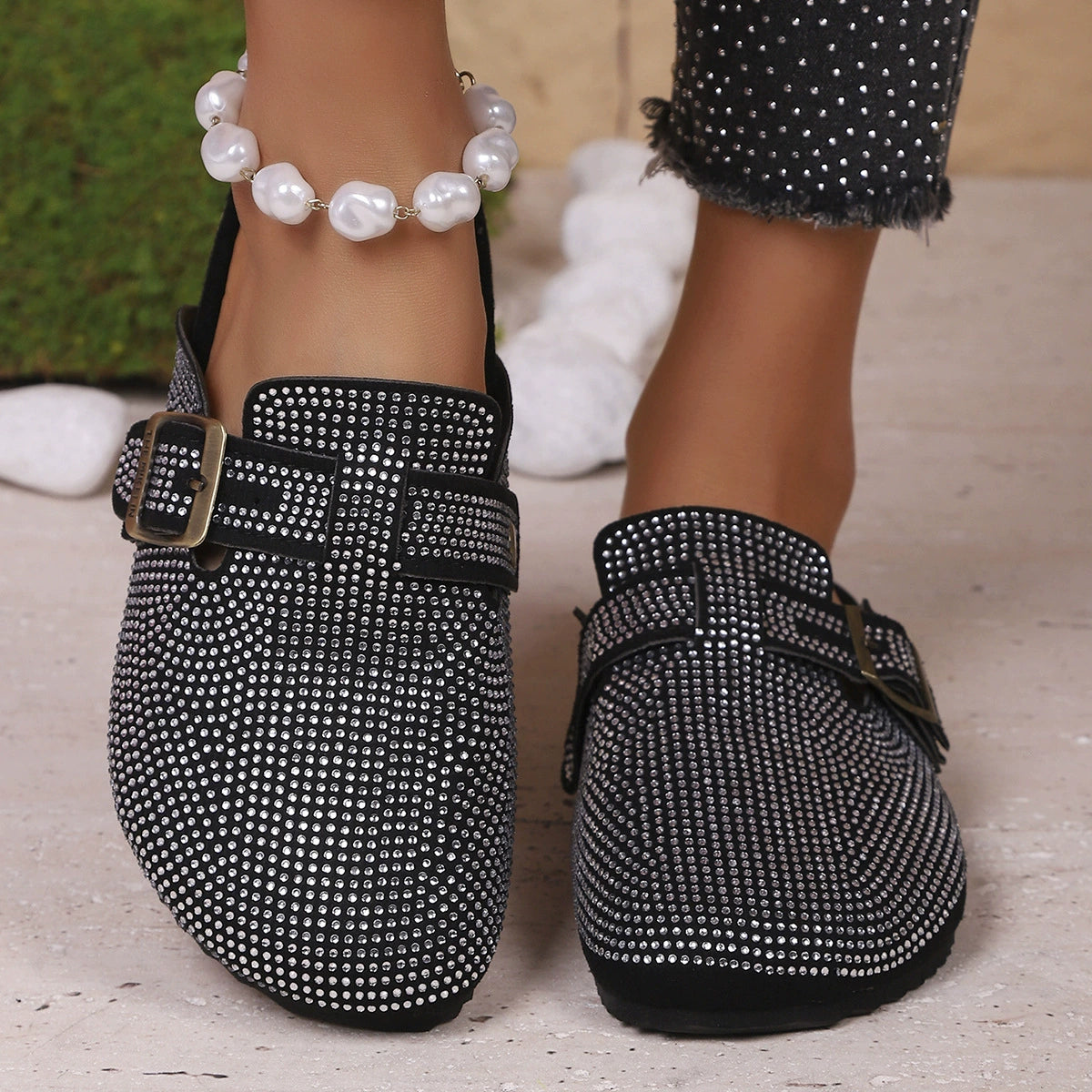 Black rhinestone buckle slip-on mules with adjustable strap and buckle detail.