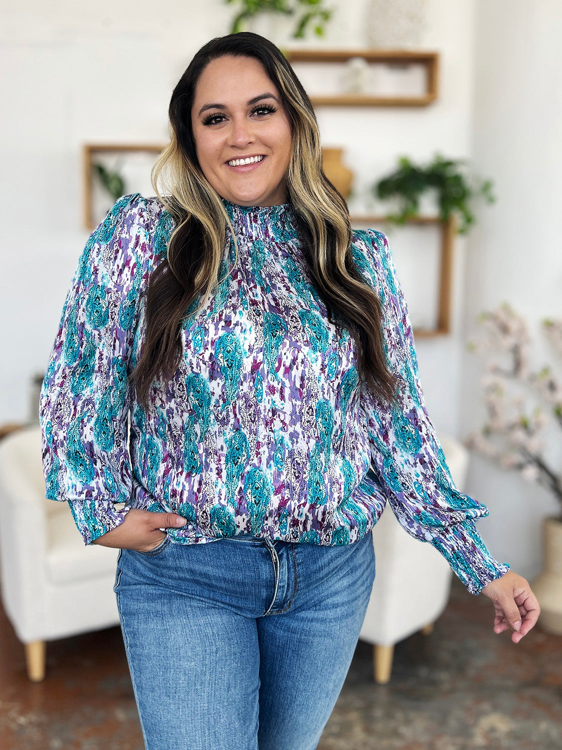 High neck abstract print blouse with smocked cuffs and hem in teal, purple, and white.
