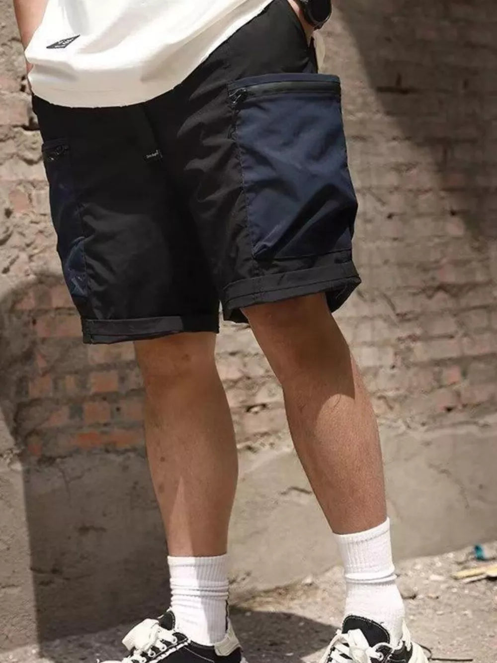 Black cargo shorts with zippered navy blue pocket detail and cuffed hem.
