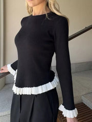 Black ribbed knit sweater with contrast white ruffled trim at hem and cuffs.