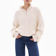 White cable knit zip-neck sweater with ribbed texture and cuffed sleeves.