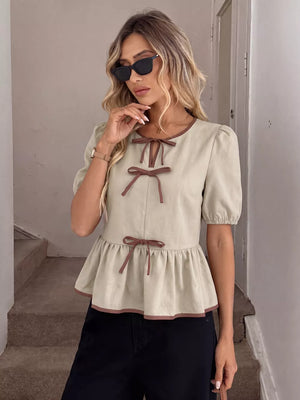 Beige V-neck blouse with brown trim and bow details, short puff sleeves, and ruffle hem.