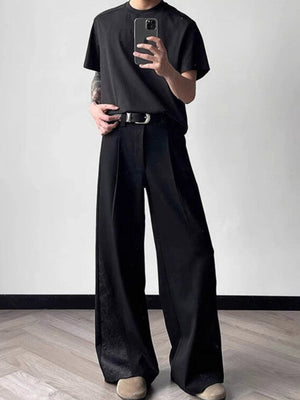 Men's black relaxed fit wide leg trousers with subtle pattern detail and a silver buckle belt.