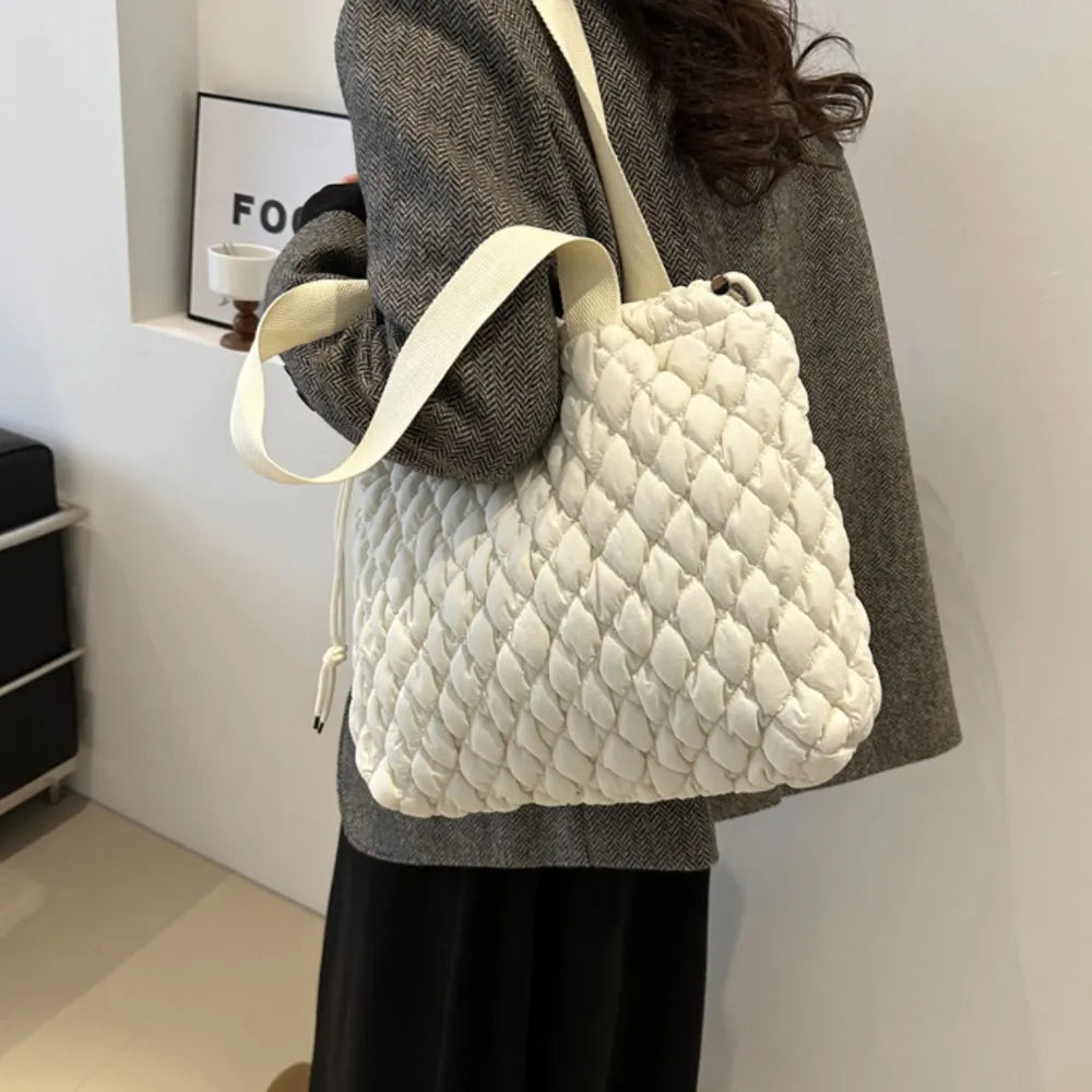 Ivory quilted drawstring carryall bag with textured pattern and fabric strap.