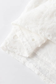 White embroidered eyelet V-neck blouse detail showing intricate floral patterns and eyelet cutouts.