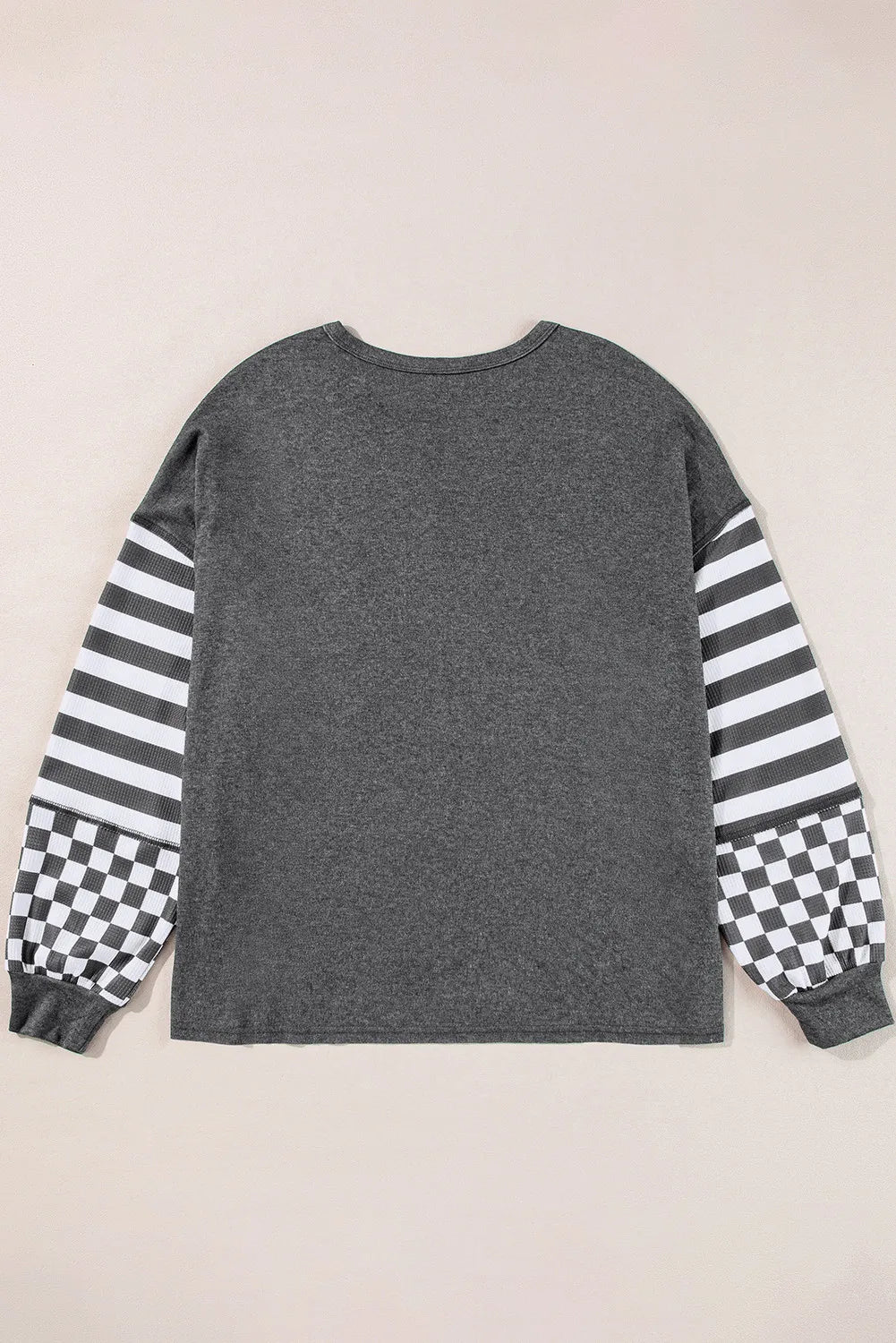Asymmetrical knit top in charcoal gray with striped and checkered patchwork sleeves.