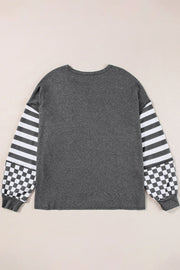 Asymmetrical knit top in charcoal gray with striped and checkered patchwork sleeves.