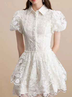 White lace mini dress with puff sleeves, button front, and tiered skirt.