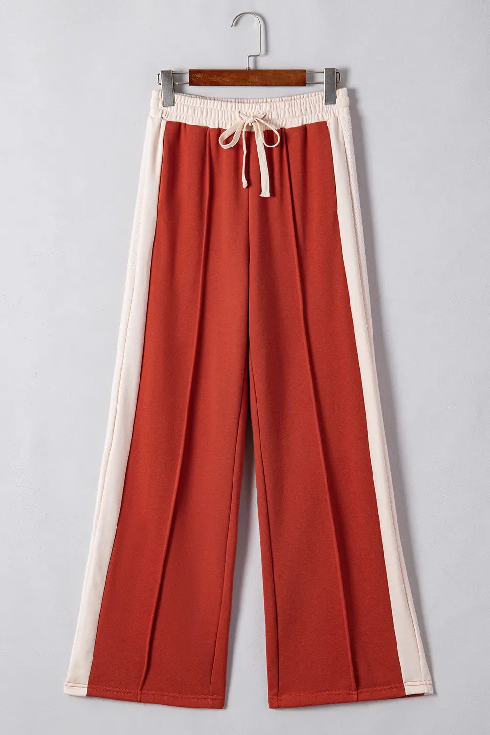 Terracotta-red track pants with cream side panels and drawstring waist