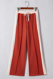 Terracotta-red track pants with cream side panels and drawstring waist