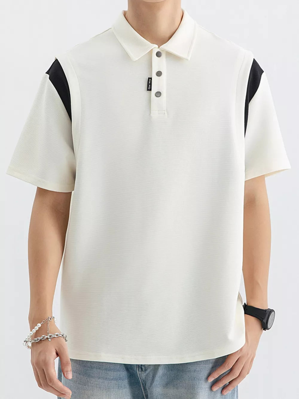 Men's beige cotton polo with black contrast shoulder panels and buttoned placket.