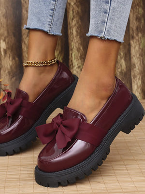Burgundy patent platform loafers with bow detail and chunky sole.