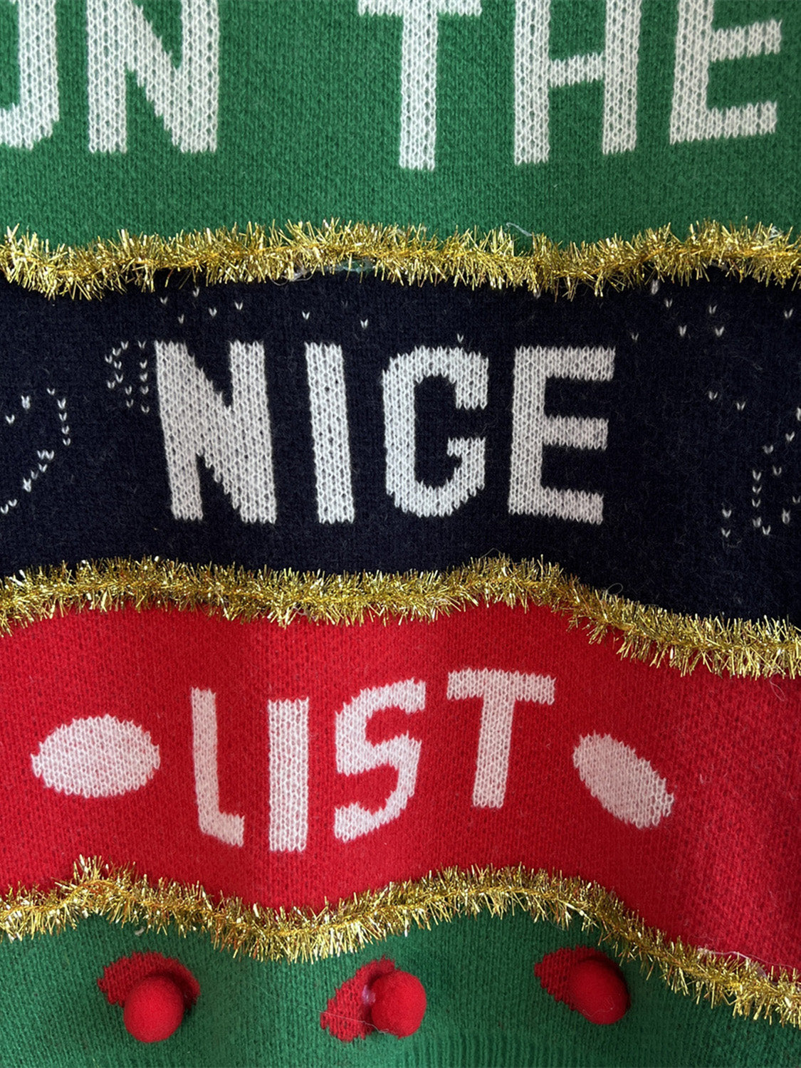 Green acrylic crewneck sweater with "Nice List" graphic and gold tinsel trim.