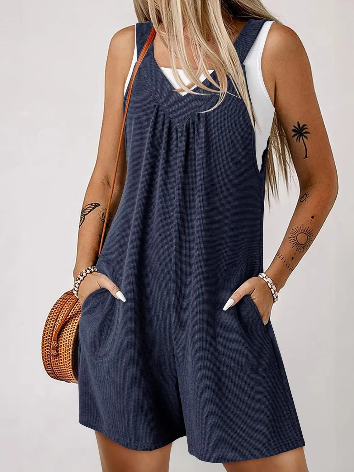 Dark blue textured romper with gathered yoke and pockets, styled with a white tank top.