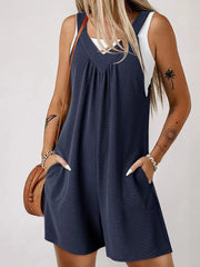 Dark blue textured romper with gathered yoke and pockets, styled with a white tank top.