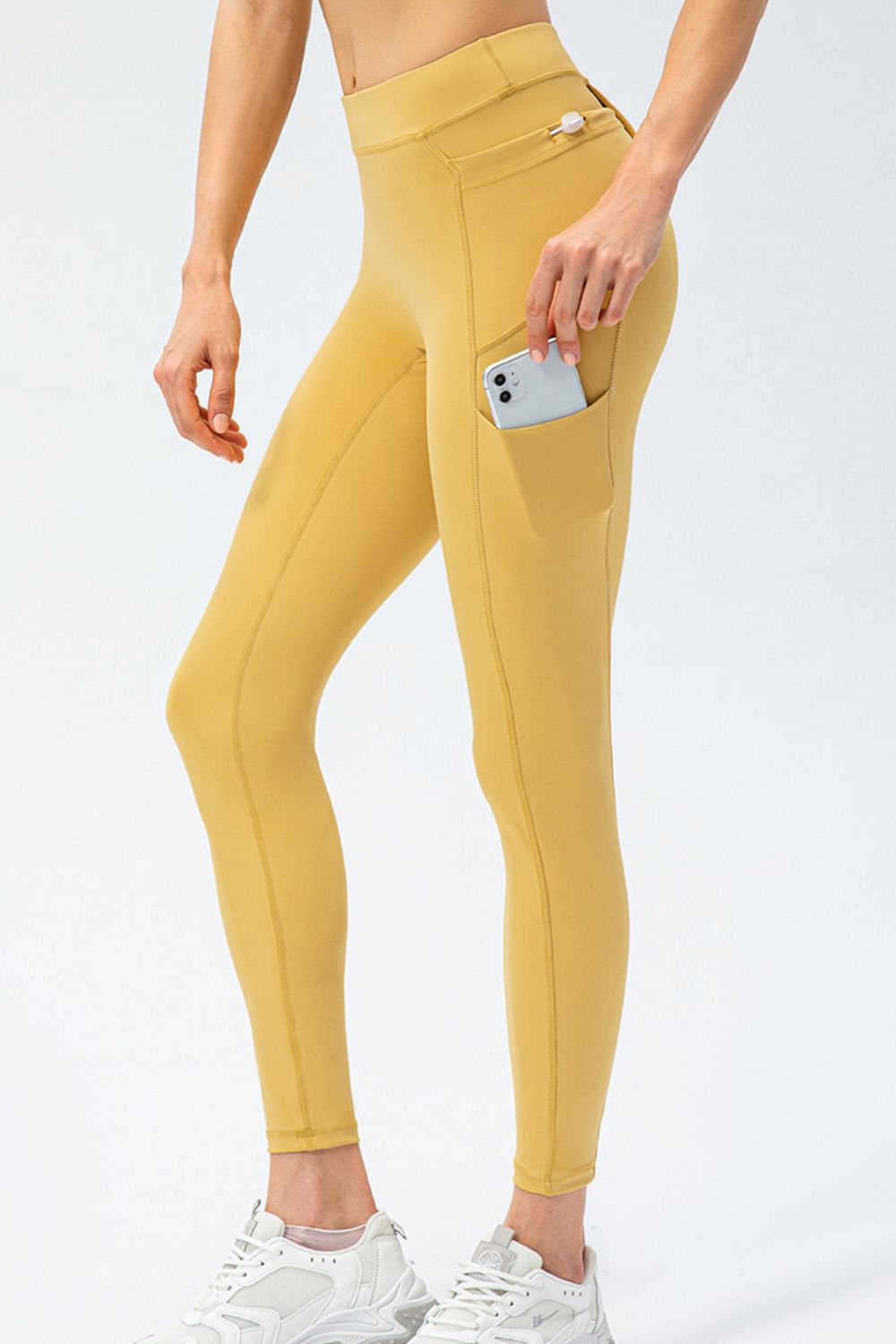 Gold athletic leggings with utility pockets, one holding a phone.