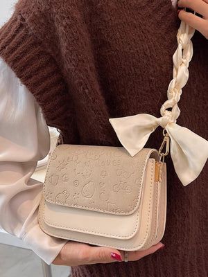 Mini two-tone crossbody bag in beige with embossed playful icons and a braided ribbon strap.