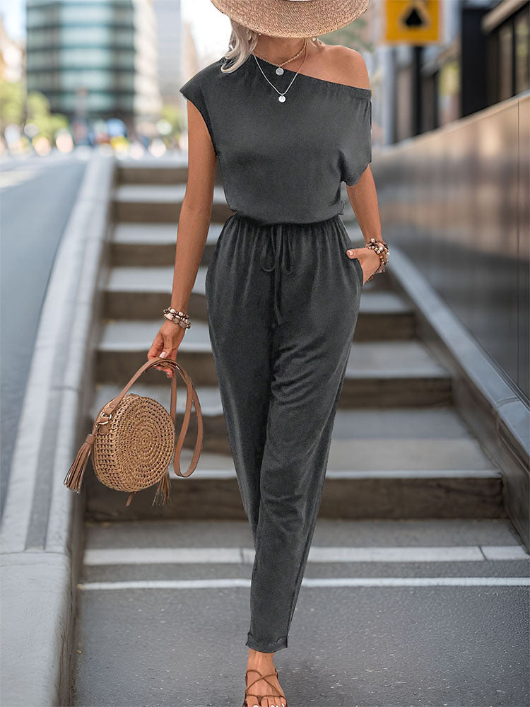 Dark gray asymmetric drape jumpsuit with drawstring waist and cap sleeves.