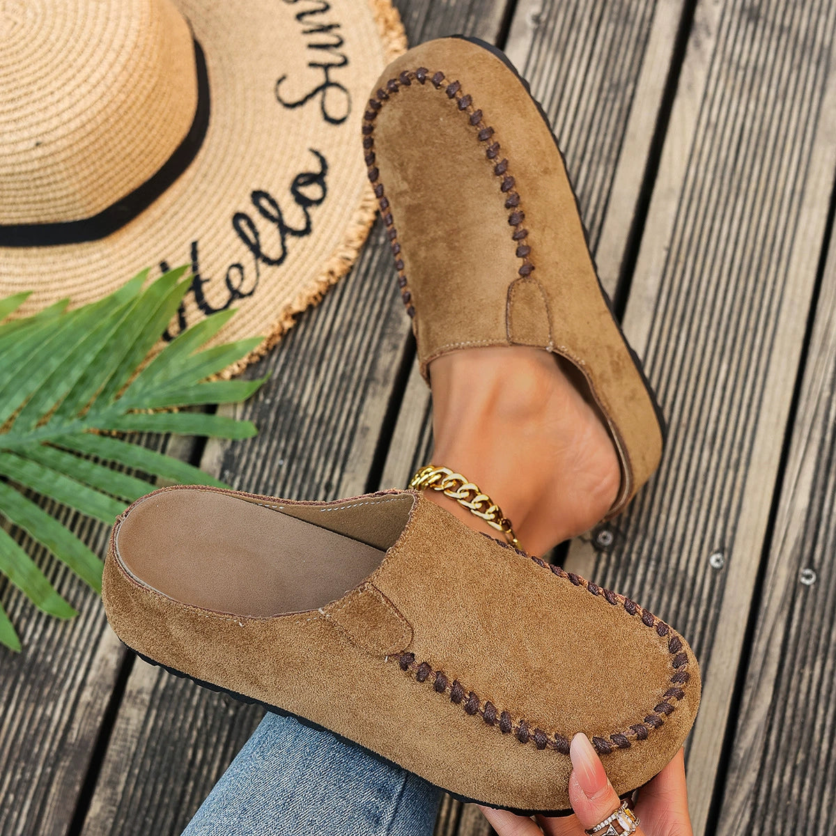 Brown suede slip-on flats with decorative stitching and a gold chain detail.