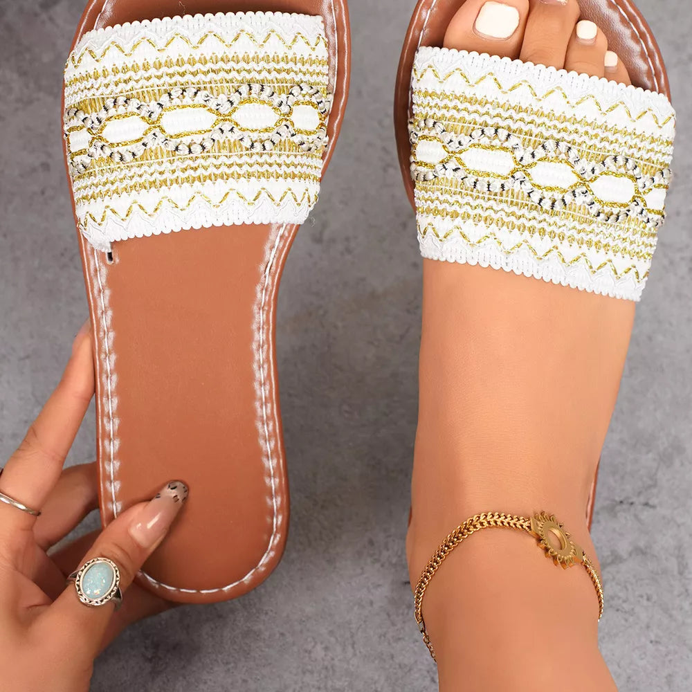 White embroidered artisan open-toe sandals with gold detailing and brown soles.