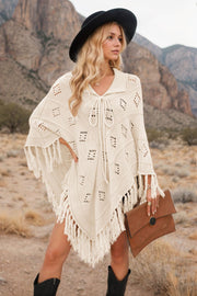 Cream knit poncho with geometric pattern and fringe, tie neck, styled with hat and clutch