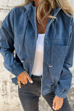 Dusty blue corduroy bomber hoodie with relaxed fit, zip front, drawstring hood, and chest pockets.