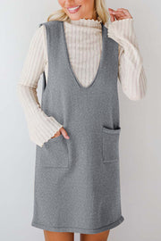 Sleeveless gray knit dress with V-neck and two front pockets, layered over a cream ribbed turtleneck.