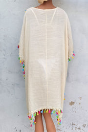 Beige kaftan dress with crochet yoke and colorful tassel trim.