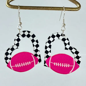 Heart-shaped acrylic earrings with pink football and black and white checkerboard pattern.