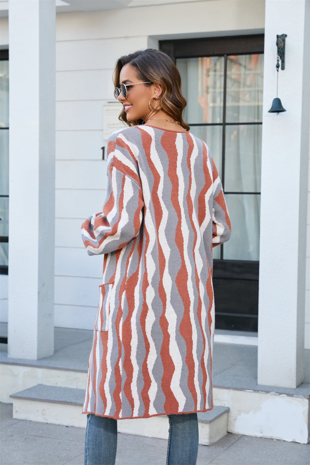 Longline knit cardigan with wave stripe pattern in rust, grey, and white. Features pockets and a relaxed fit.