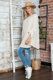 Cream knit sweater with cape sleeves and a relaxed fit, styled with distressed jeans.