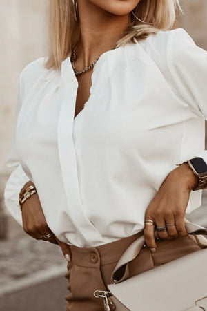 White pleated yoke blouse with button detail and V-neckline.