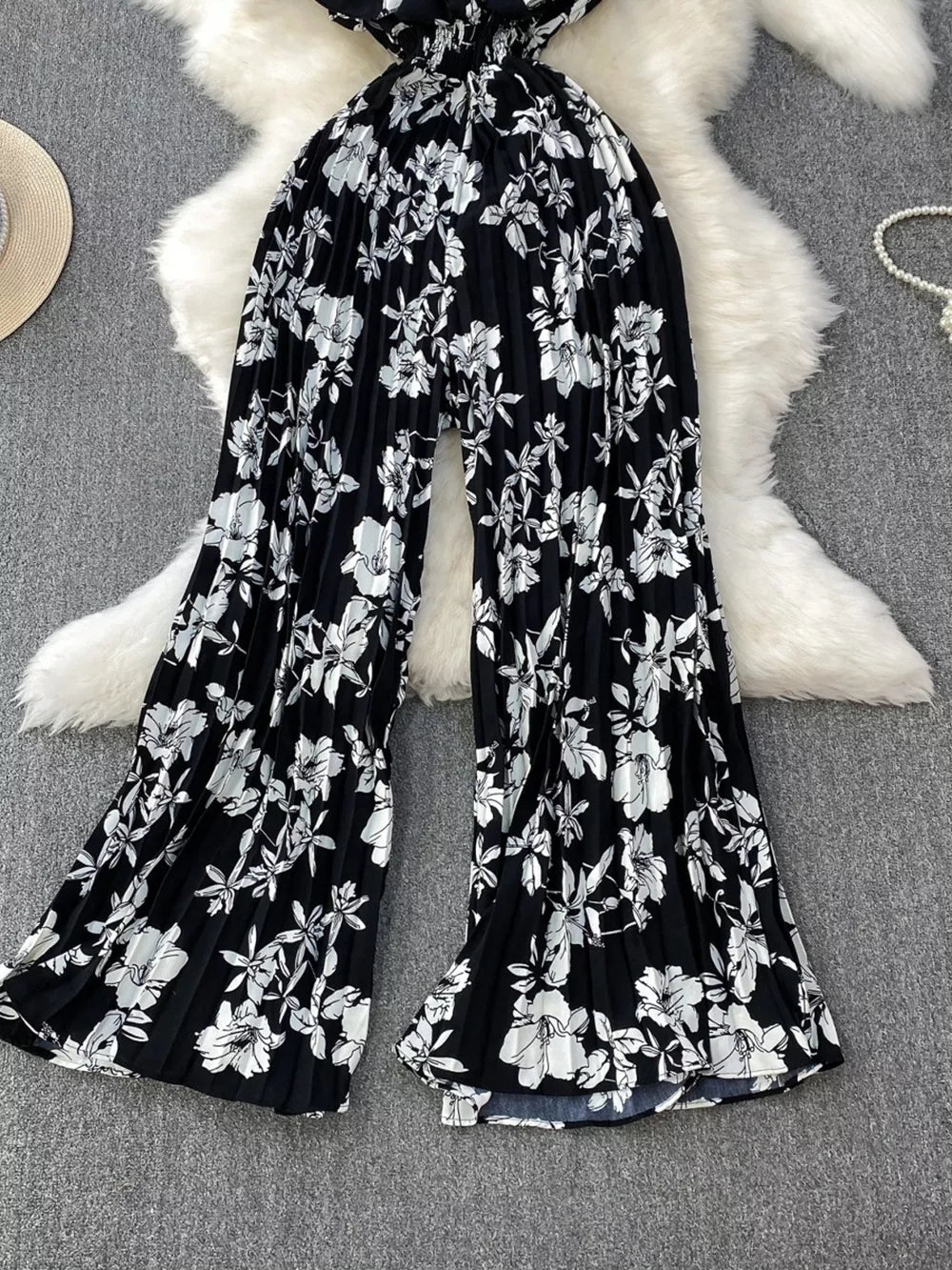 Black floral pleated wide-leg romper with a smocked waist and flowing legs.