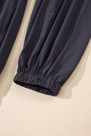 Dark gray jumpsuit with gathered elastic ankle cuffs and drawstring waist detail.