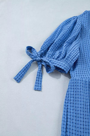 Blue midi dress with checkered pattern, puff sleeves, and tie cuffs.