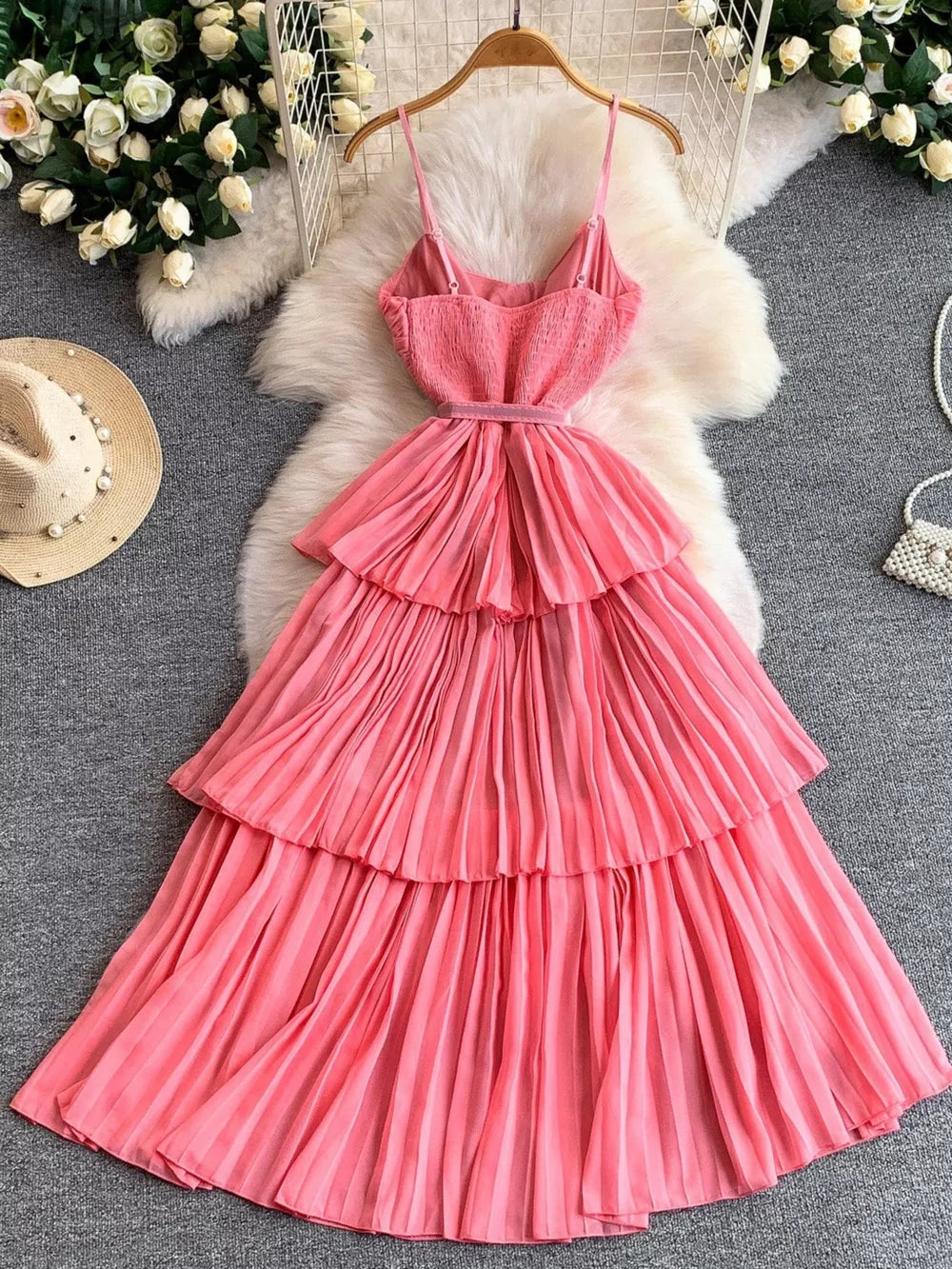 Pink belted midi dress with spaghetti straps, smocked bodice, and tiered pleated skirt.
