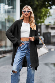 Black open-knit longline cardigan with side slits and textured details, worn open over a white crop top and jeans.