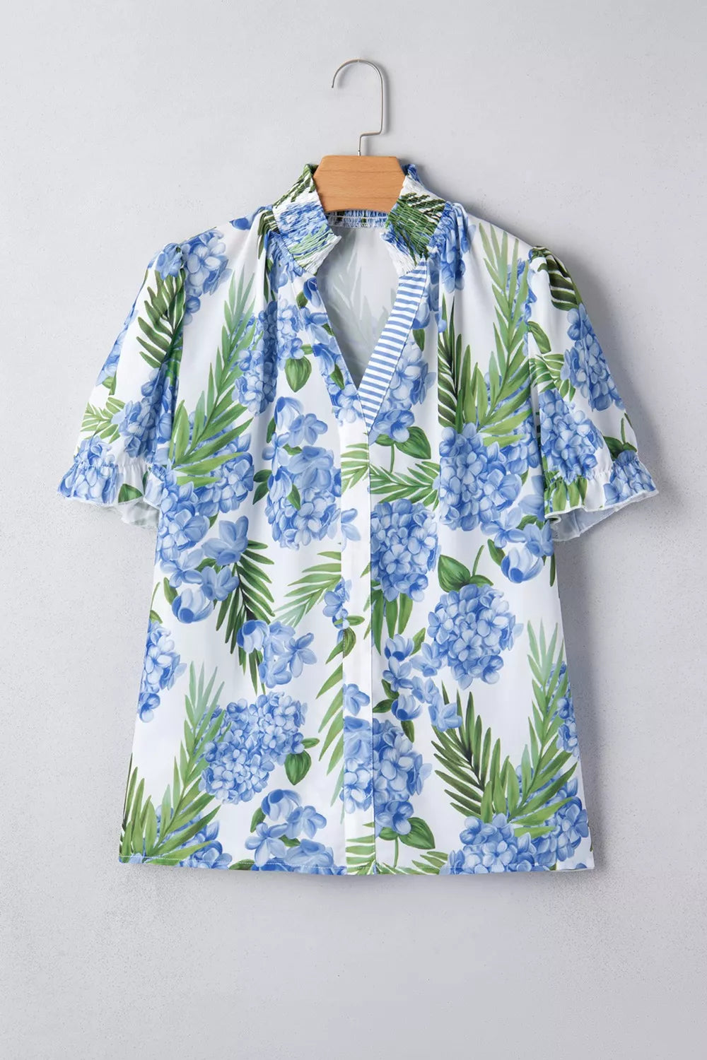 White V-neck blouse with blue hydrangea floral print, ruffled short sleeves, and smocked collar.