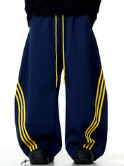 Men's navy blue wide-leg sweatpants with yellow side stripes and drawstring waist.