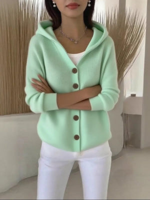 Green hooded button-front knit cardigan with brown buttons, styled with a white tank and white pants.
