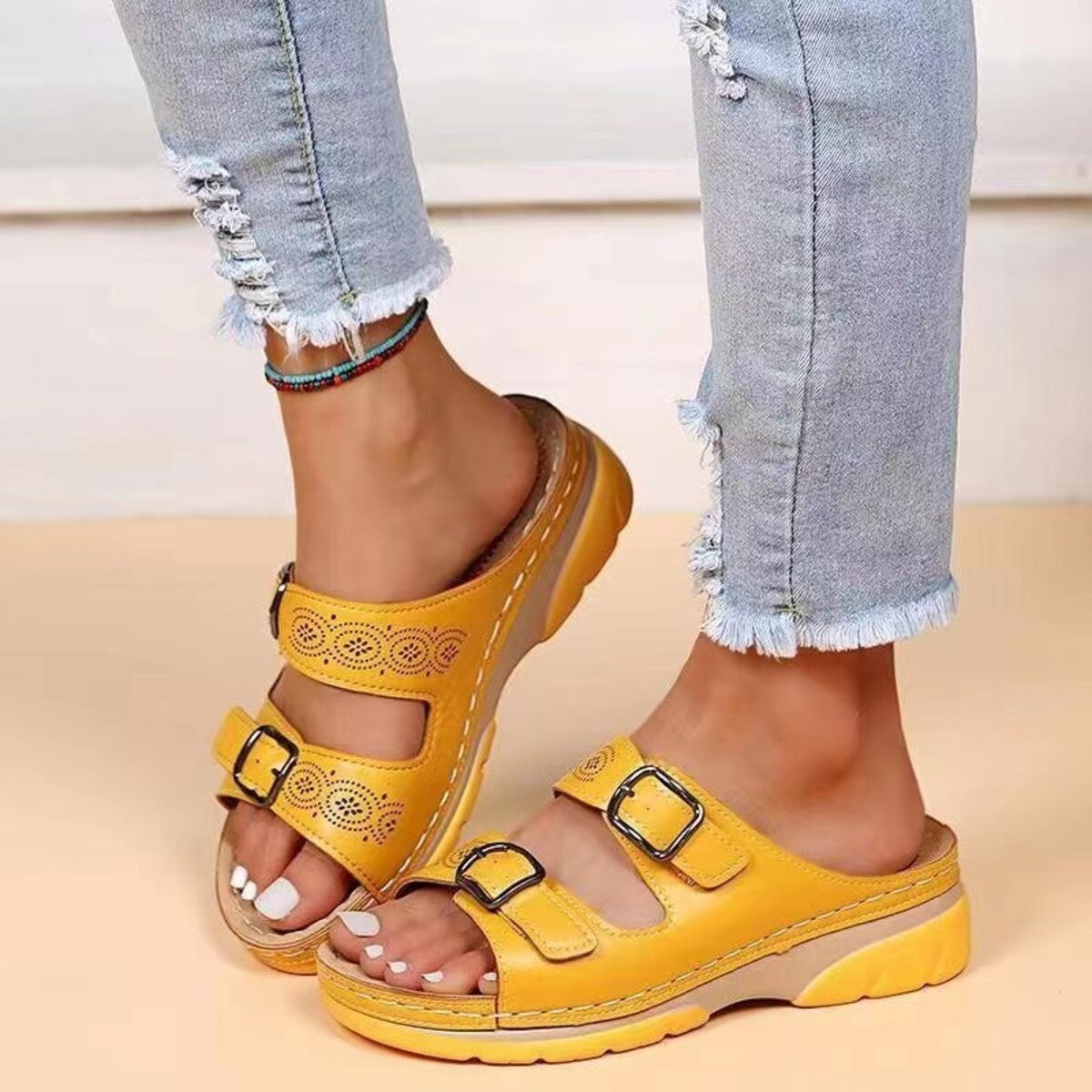Yellow open-toe sandals with double buckles and decorative cutouts.