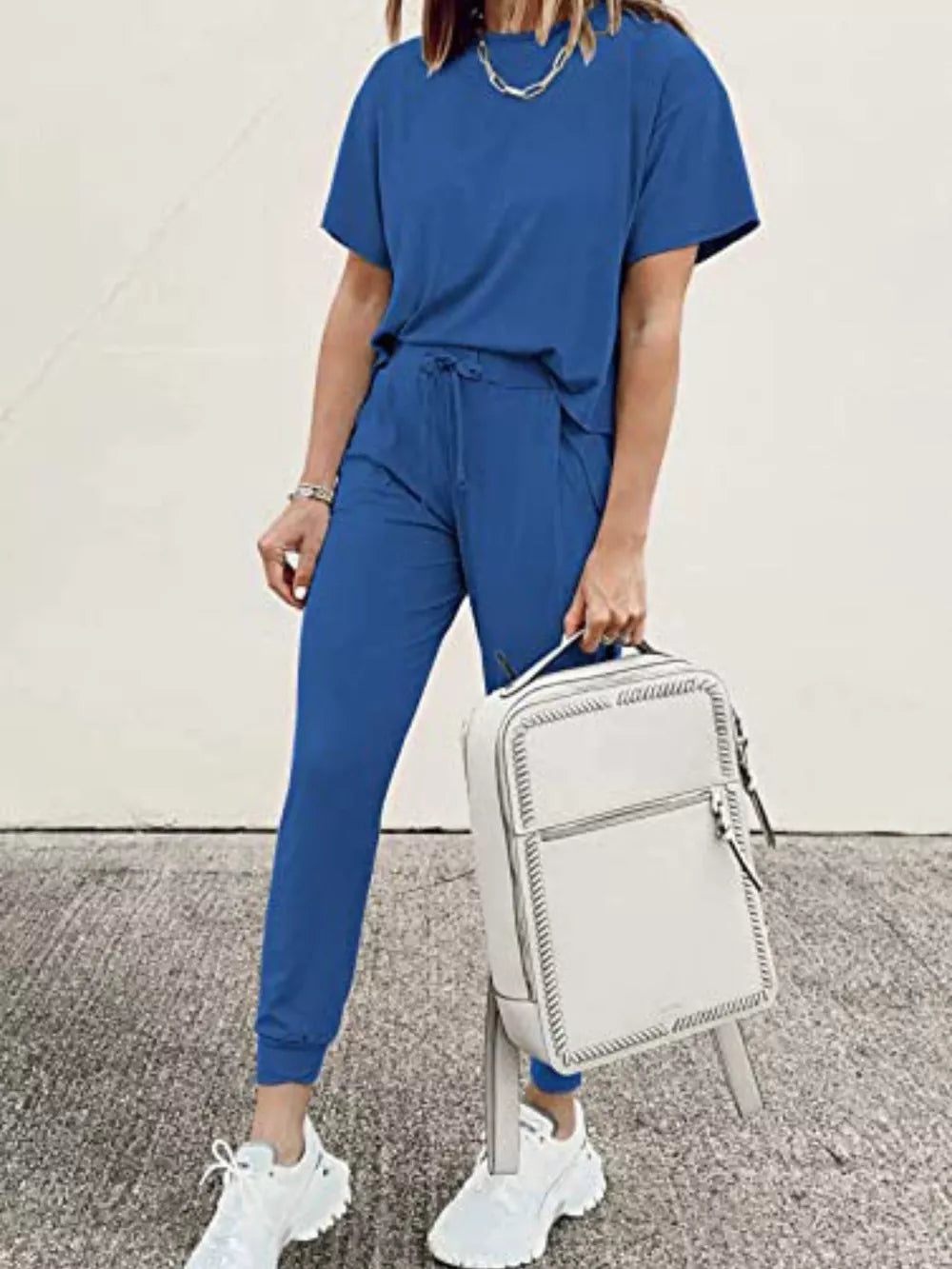 Blue casual round neck top and jogger pants set with drawstring waist, styled with white sneakers and a backpack.